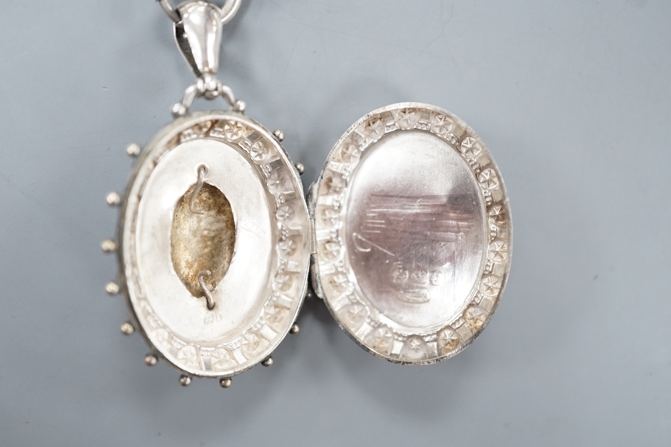 A late Victorian silver oval locket, on a white metal albertina, 49cm.